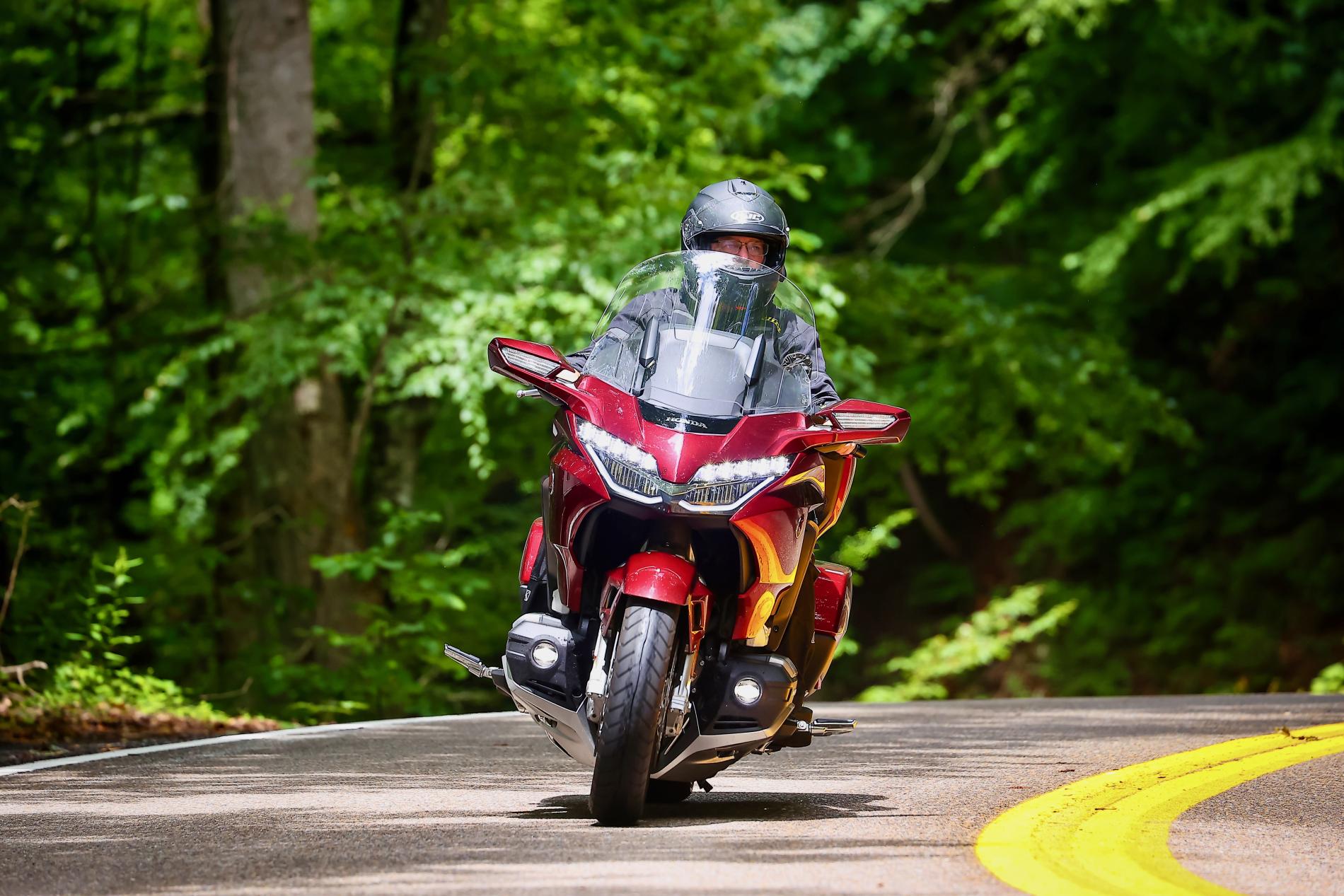 Motorcyclist on red bike rides through a lush forest road.